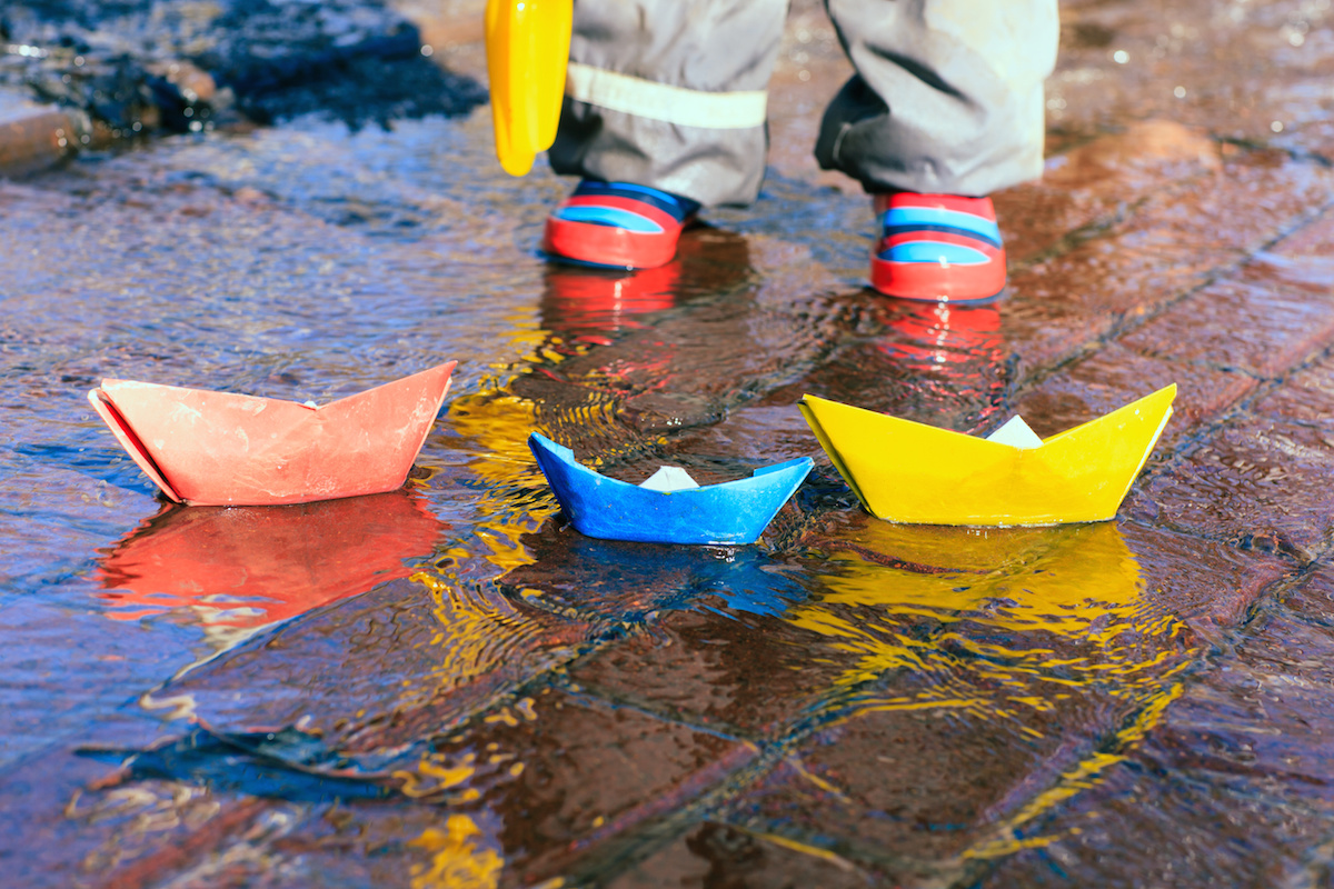 child playing with paper boats in water puddle
